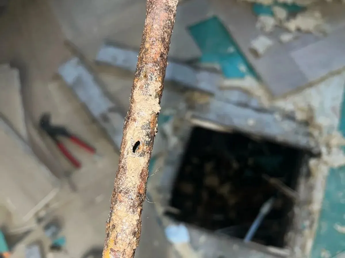 Corroded length of copper pipe held above an open hole in the floor
