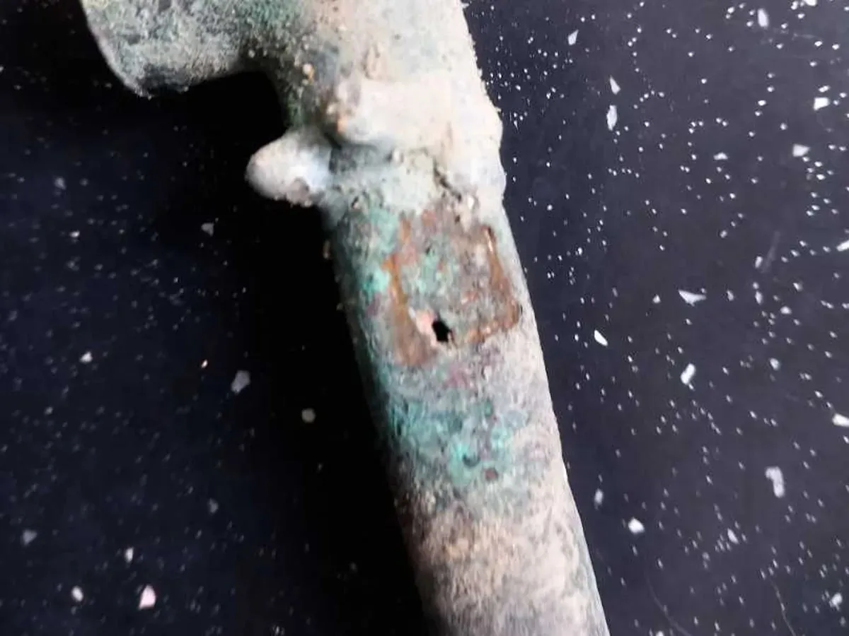 Close-up of a corroded green copper tee with a pinhole