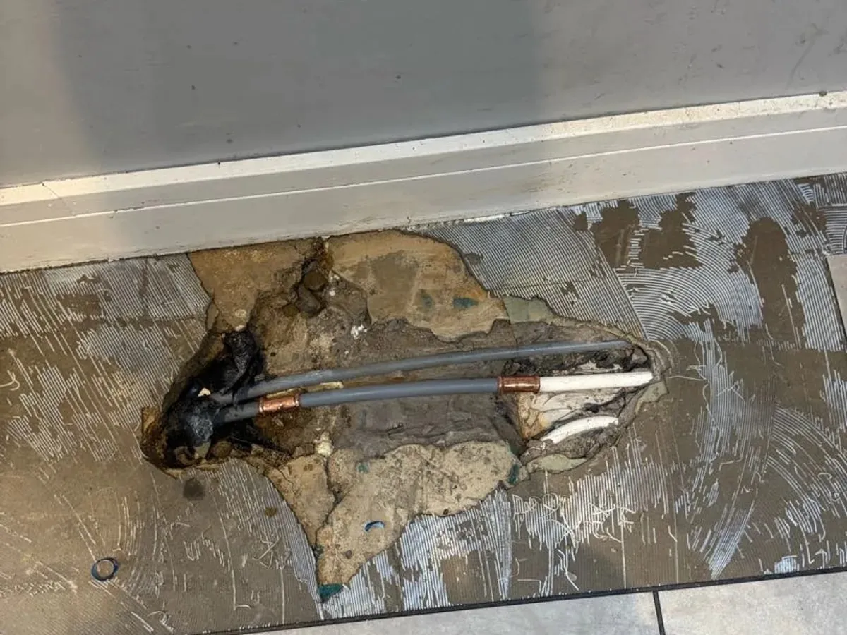 Plastic heating pipes rejoined with crimped fittings in an opened patch of floor