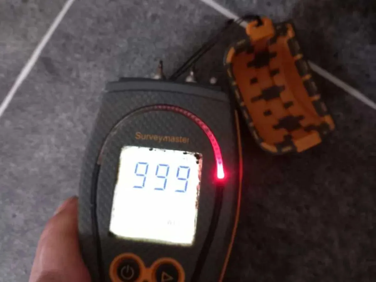 Damp meter displaying 999, its highest reading, over a kitchen floor