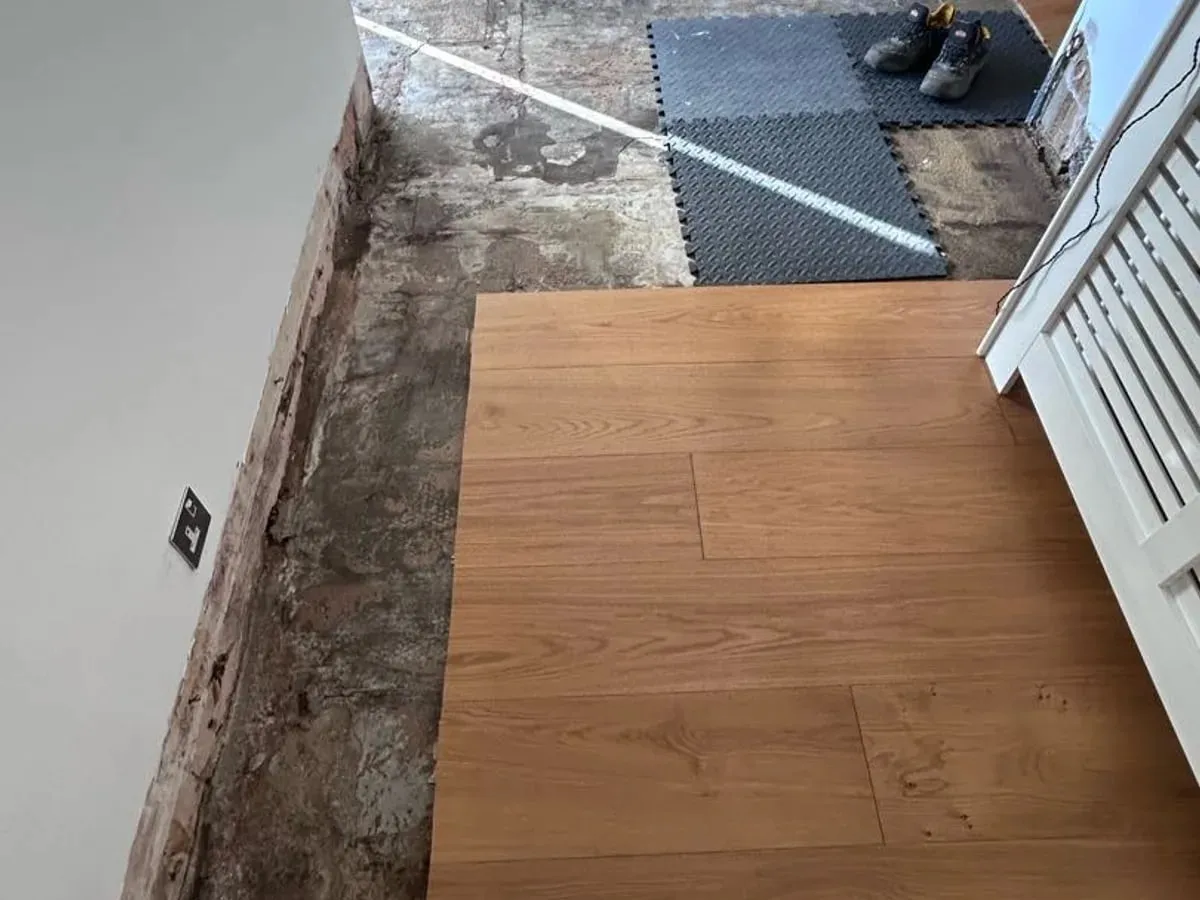 Engineered wood flooring partly lifted, showing a damp concrete subfloor