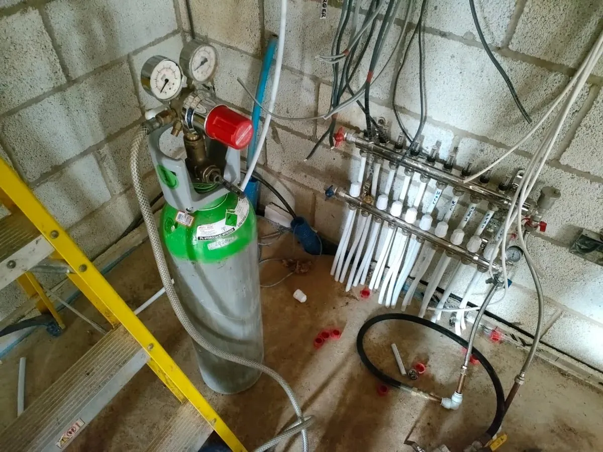 Tracer gas cylinder with regulator connected beside the underfloor heating manifold on a block wall